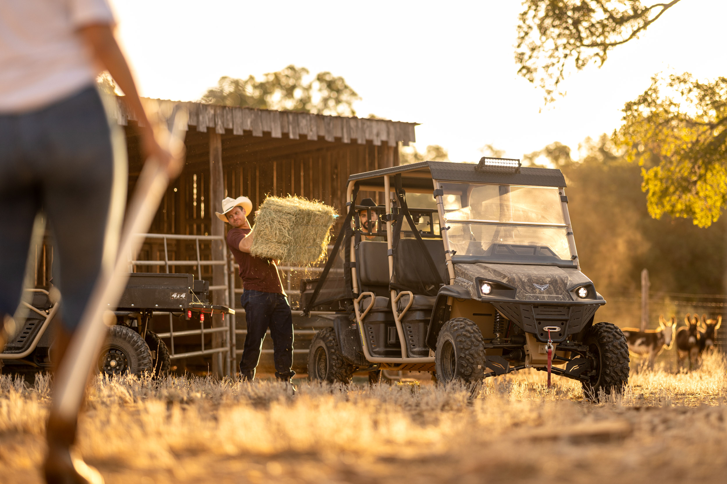 man unloading hay bale from landmaster utv with woman in foreground