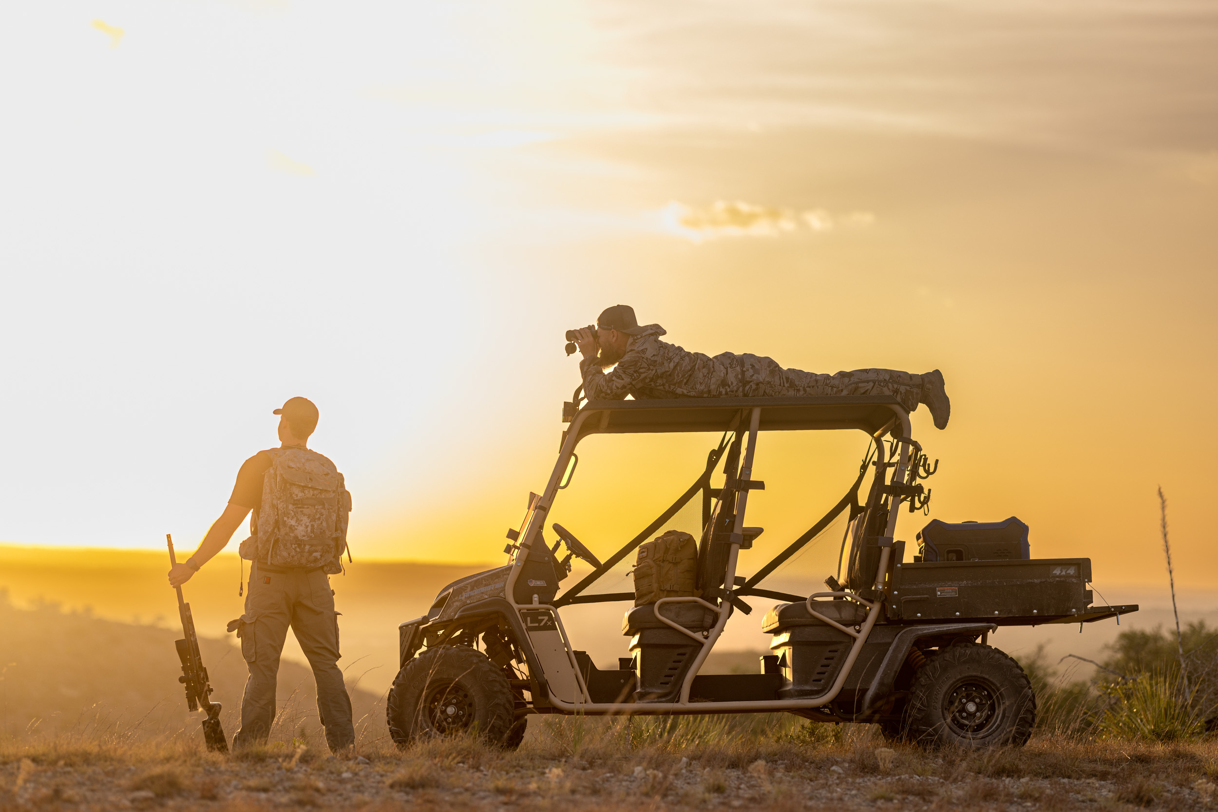 hunters on utv at sunset using binoculars and holding rifle