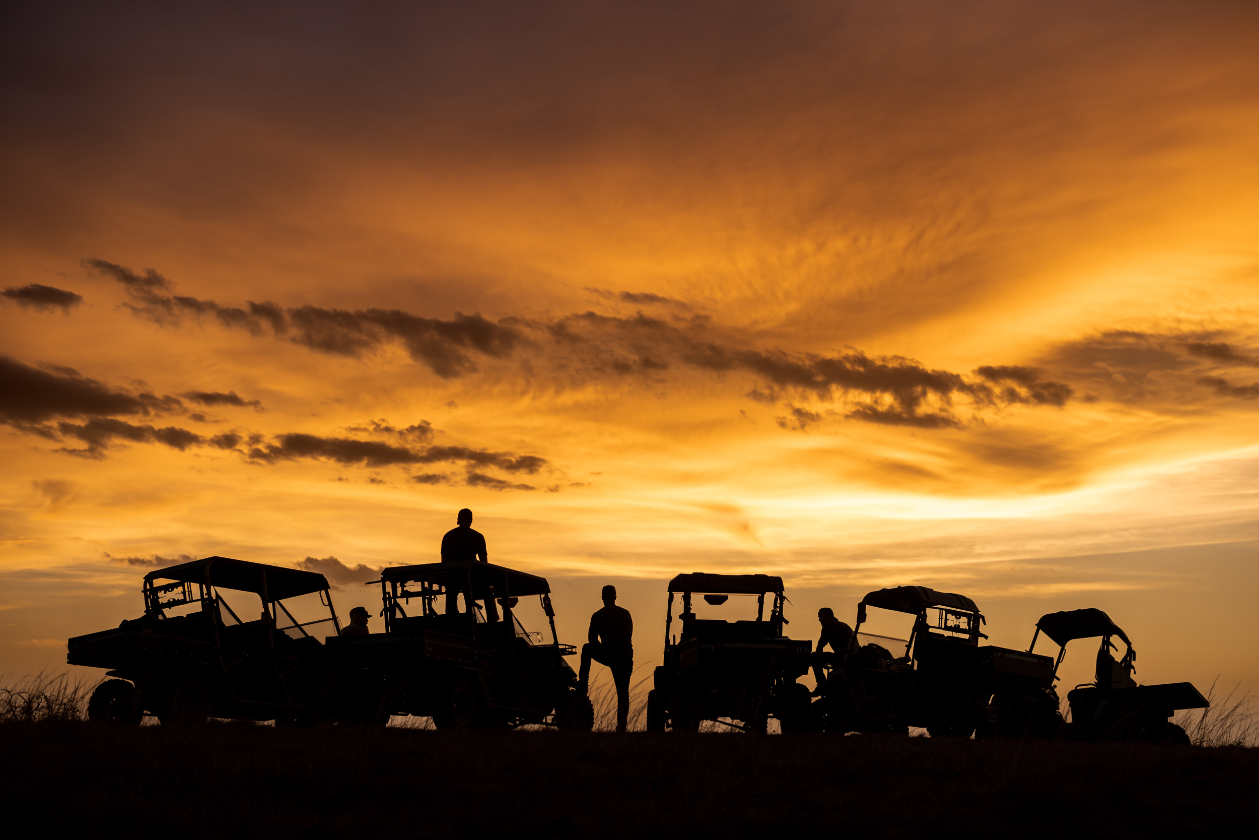 group of people and utv vehicles silhouette at sunset near cliff
