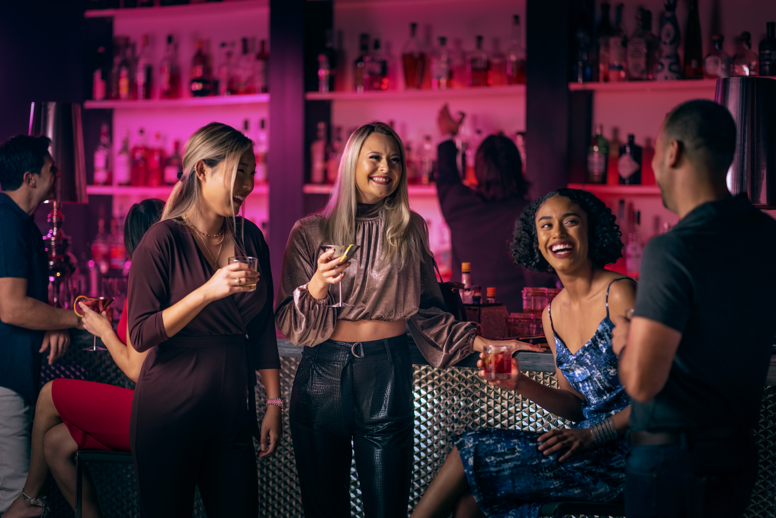 man approaches group of woman at bar with pink lighting in hotel