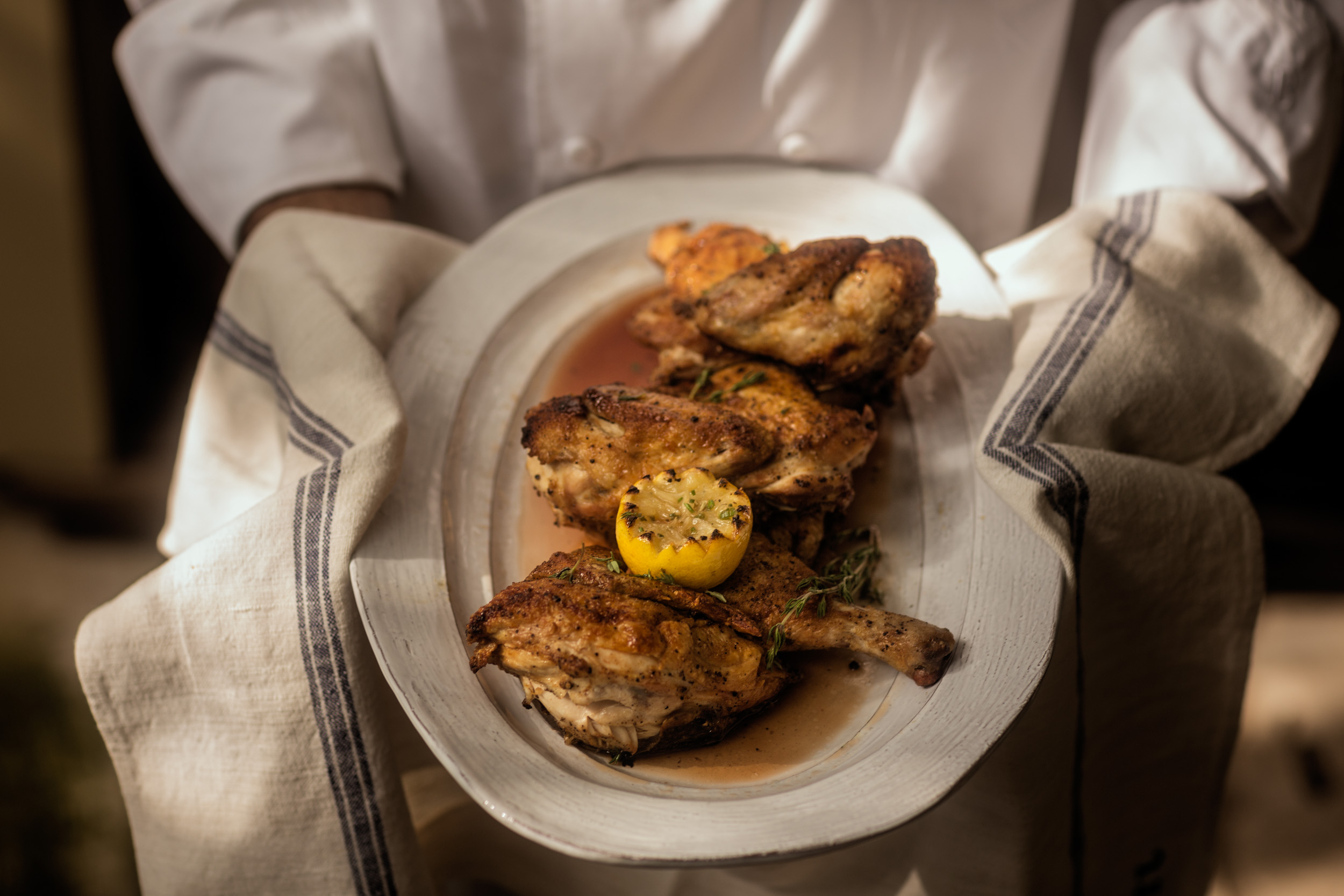 chef holding platter of roasted chicken at grilled lemons