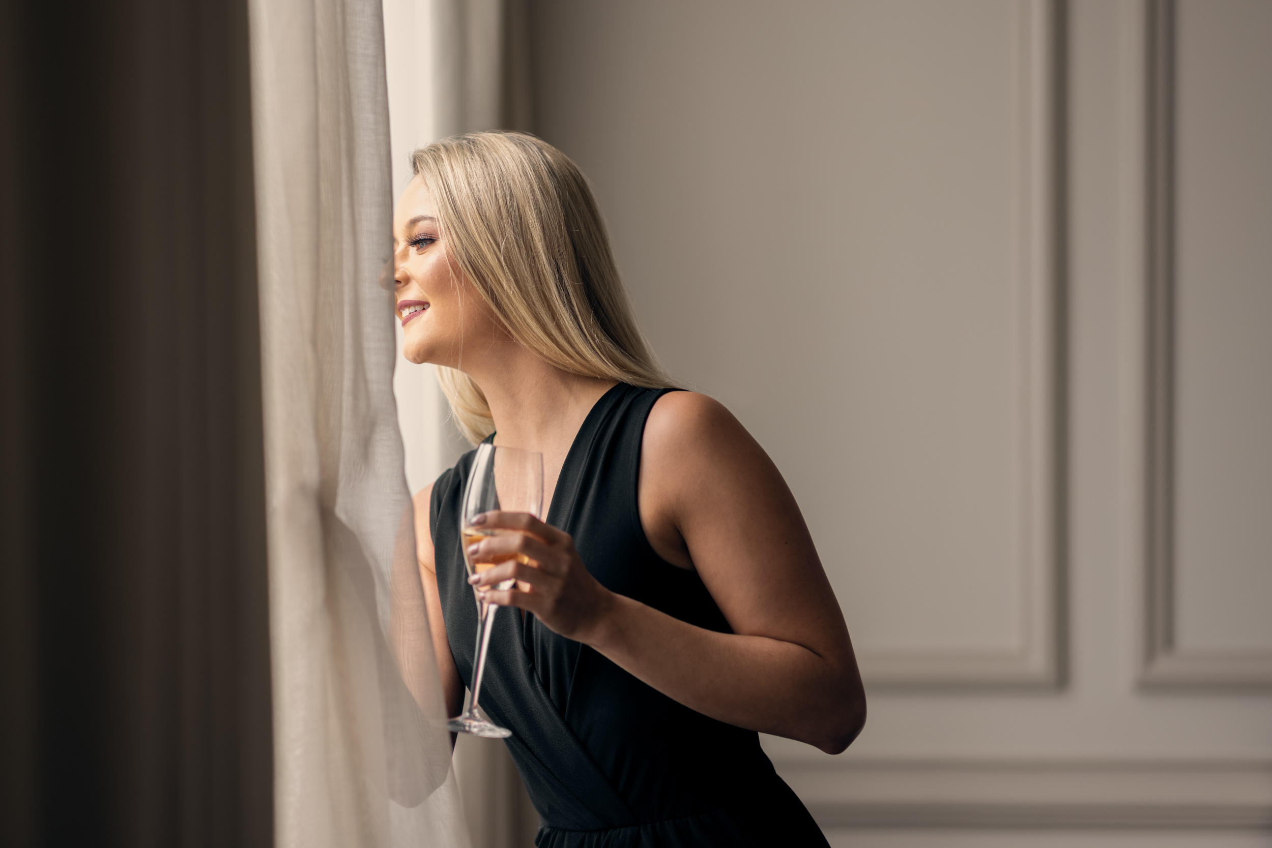 woman holding champagne glass looking out window of hotel room