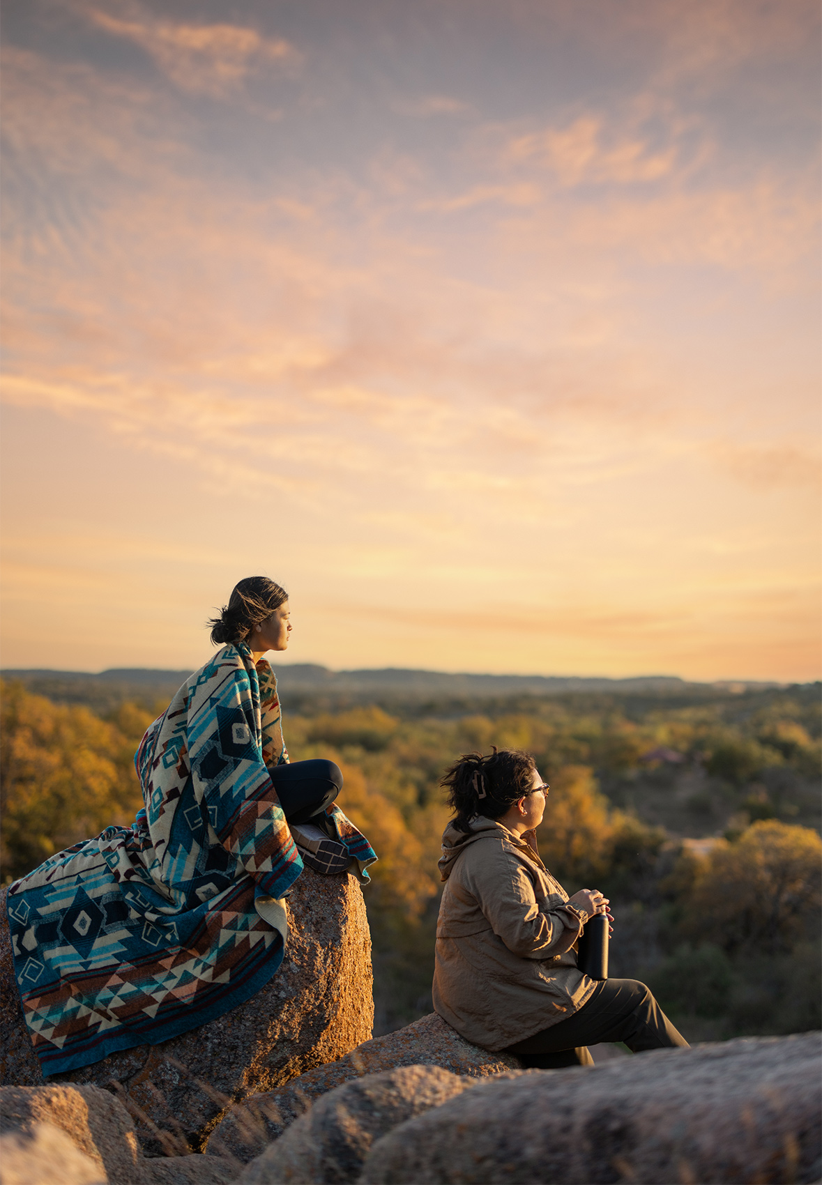mother and daughter sit and view sunset at enchanted rock state park in texas