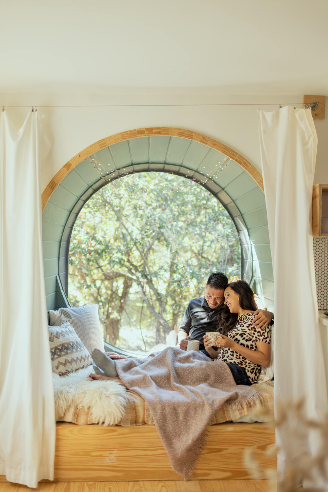 couple smiling and sitting in window nook with blankets