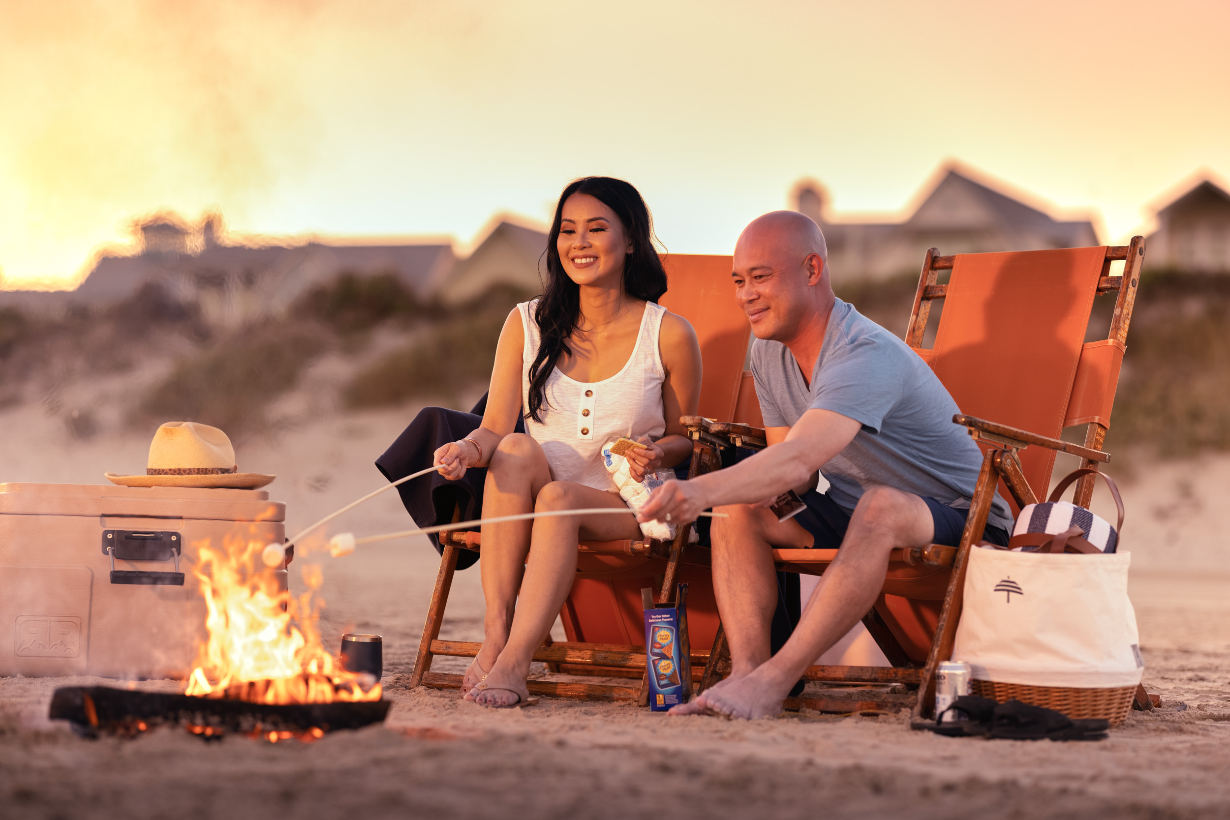 woman and man roasting marshmallows at campfire on beach