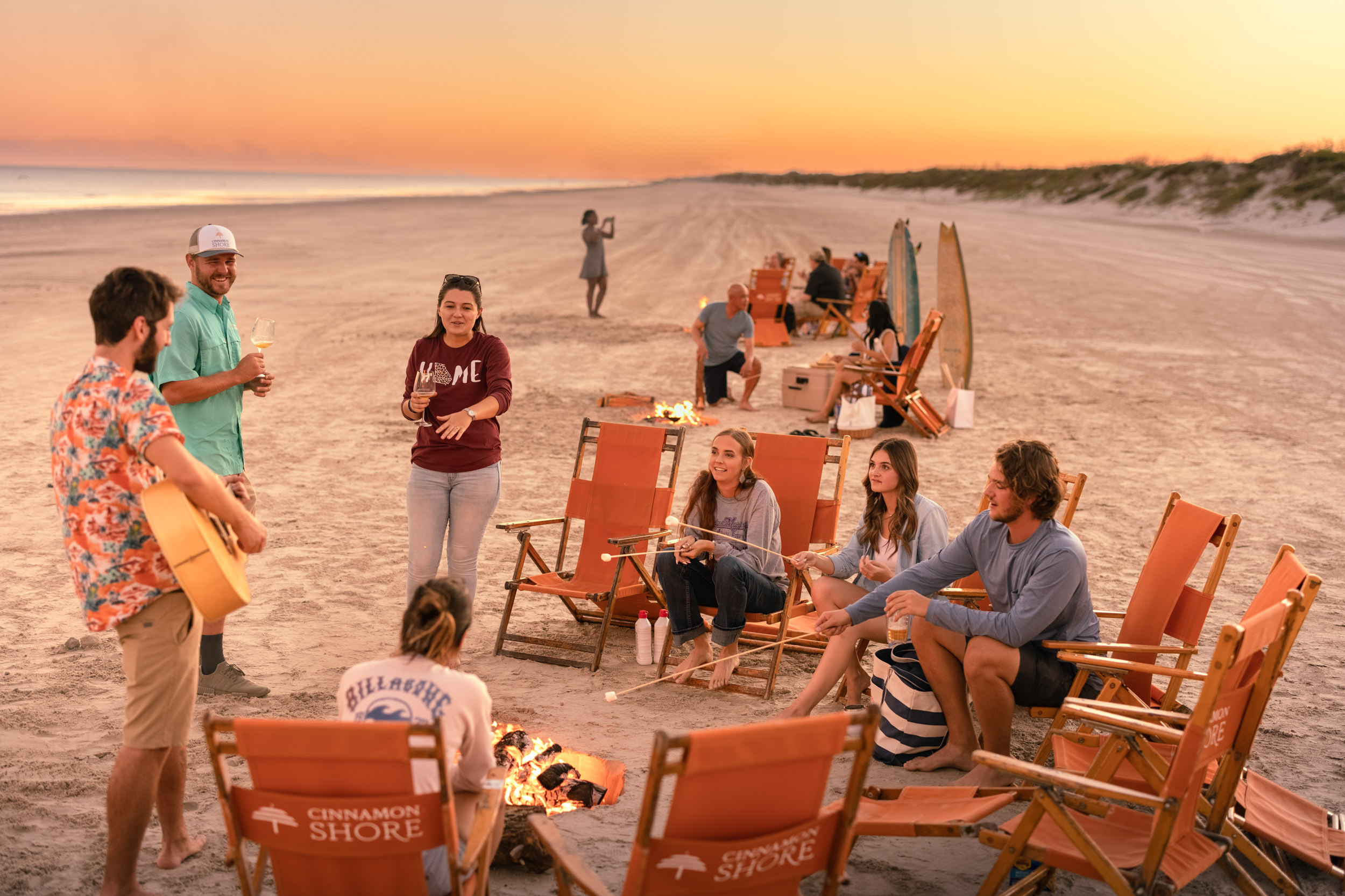 group of friends hanging out on beach with campfire at sunset