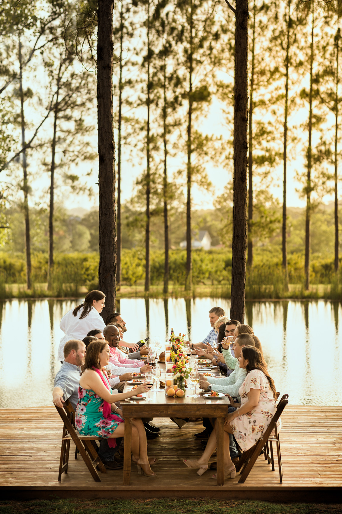 large dinner table setup on dock with pond and trees