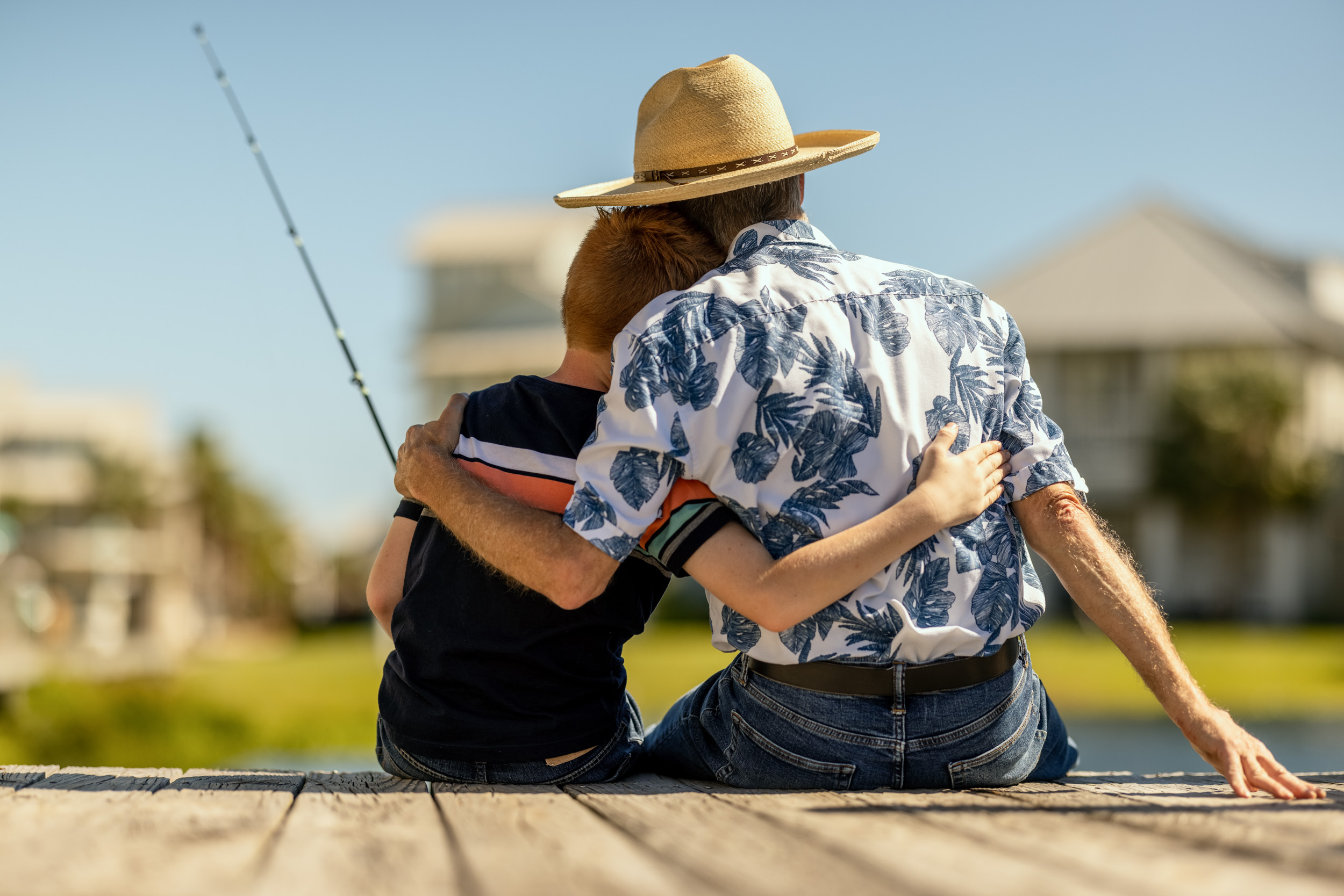 grandfather and grandson embrace while fishing on dock