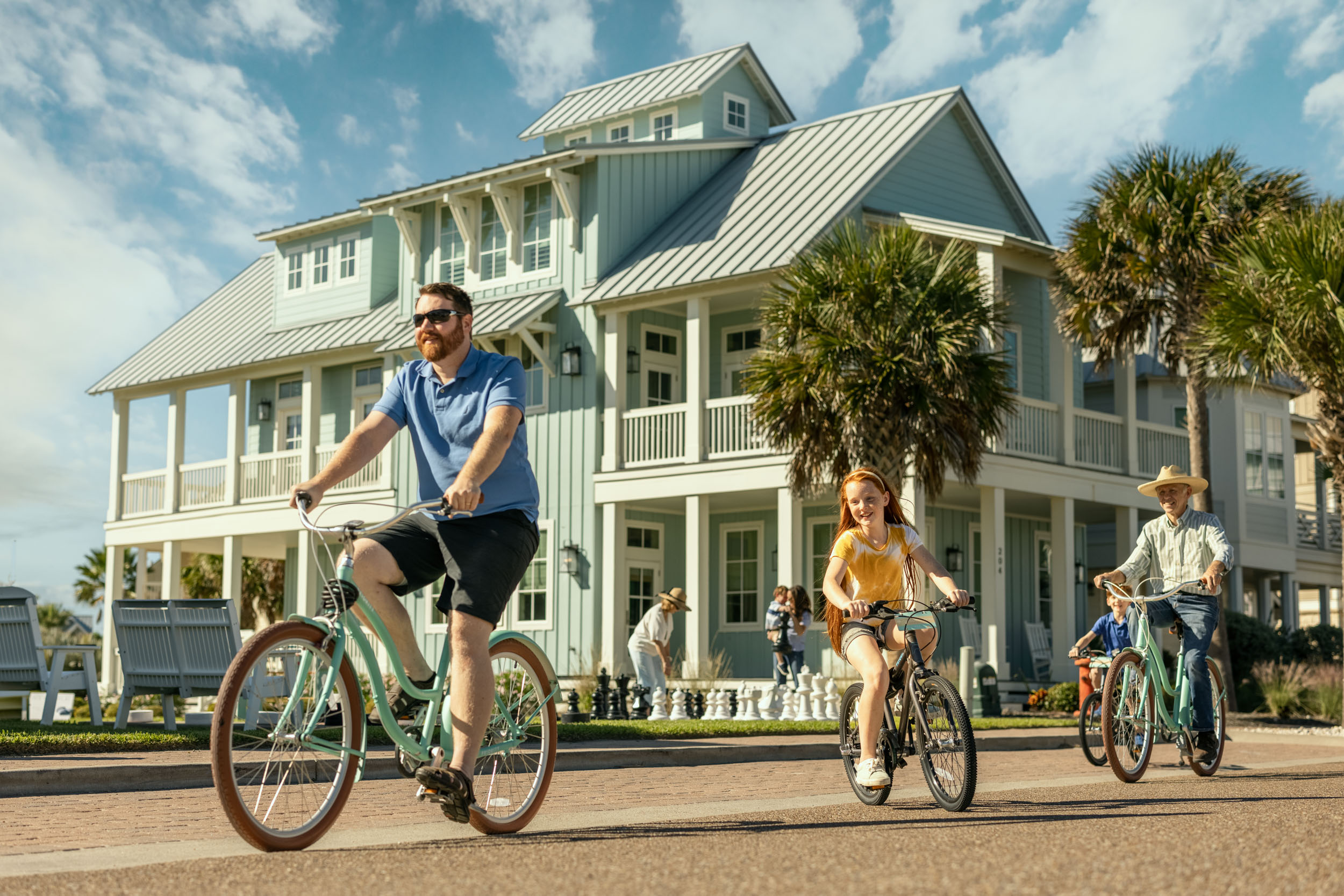 family riding bicycles in beach community with house in background