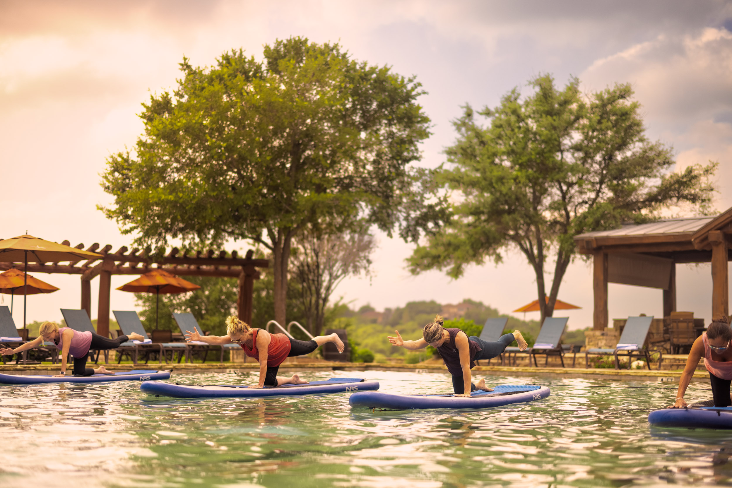 group of woman doing yoga on paddle boards in pool