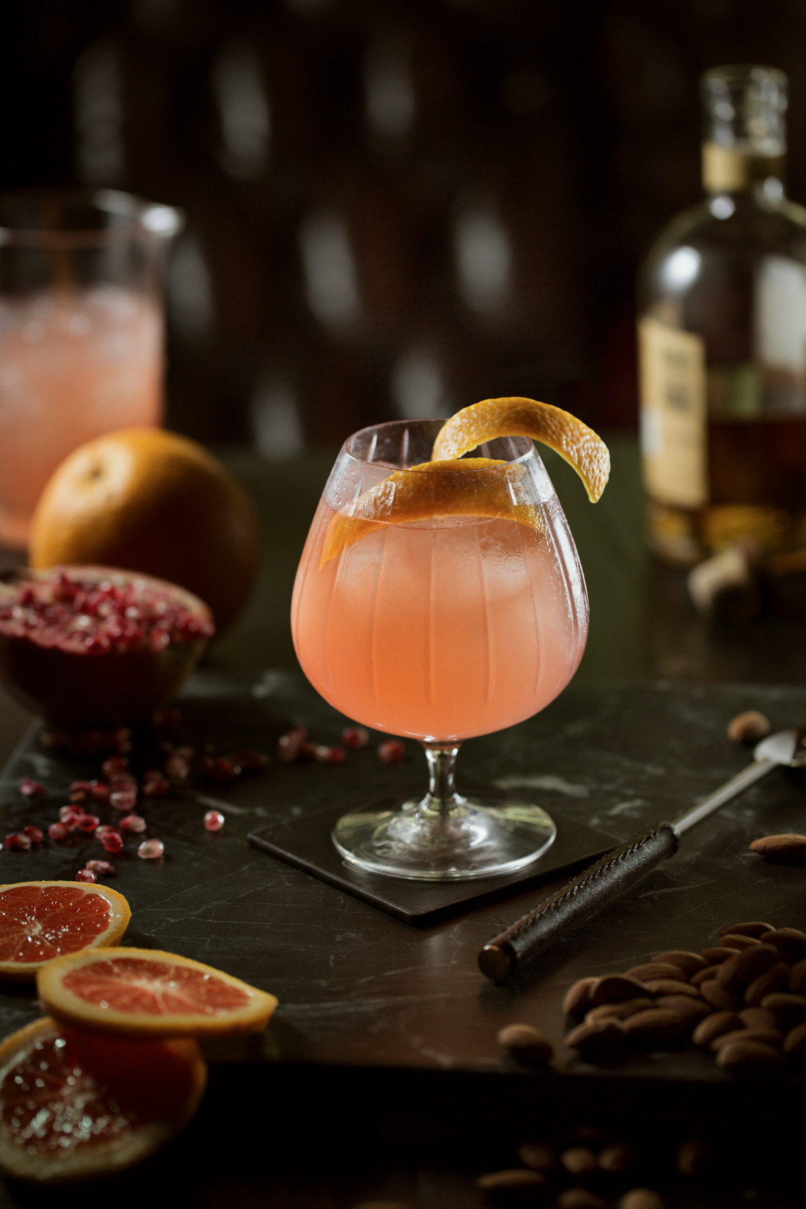 signature cocktail drink on dark surface with citrus fruits and pomegranate