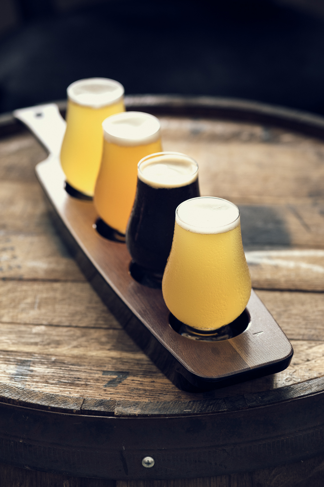 beer flight in glasses on wooden board and oak barrel