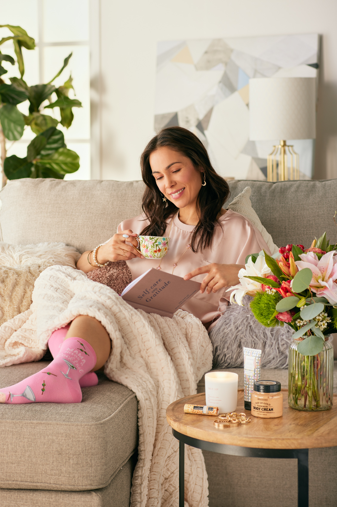 woman holding tea reading book with blanket on couch