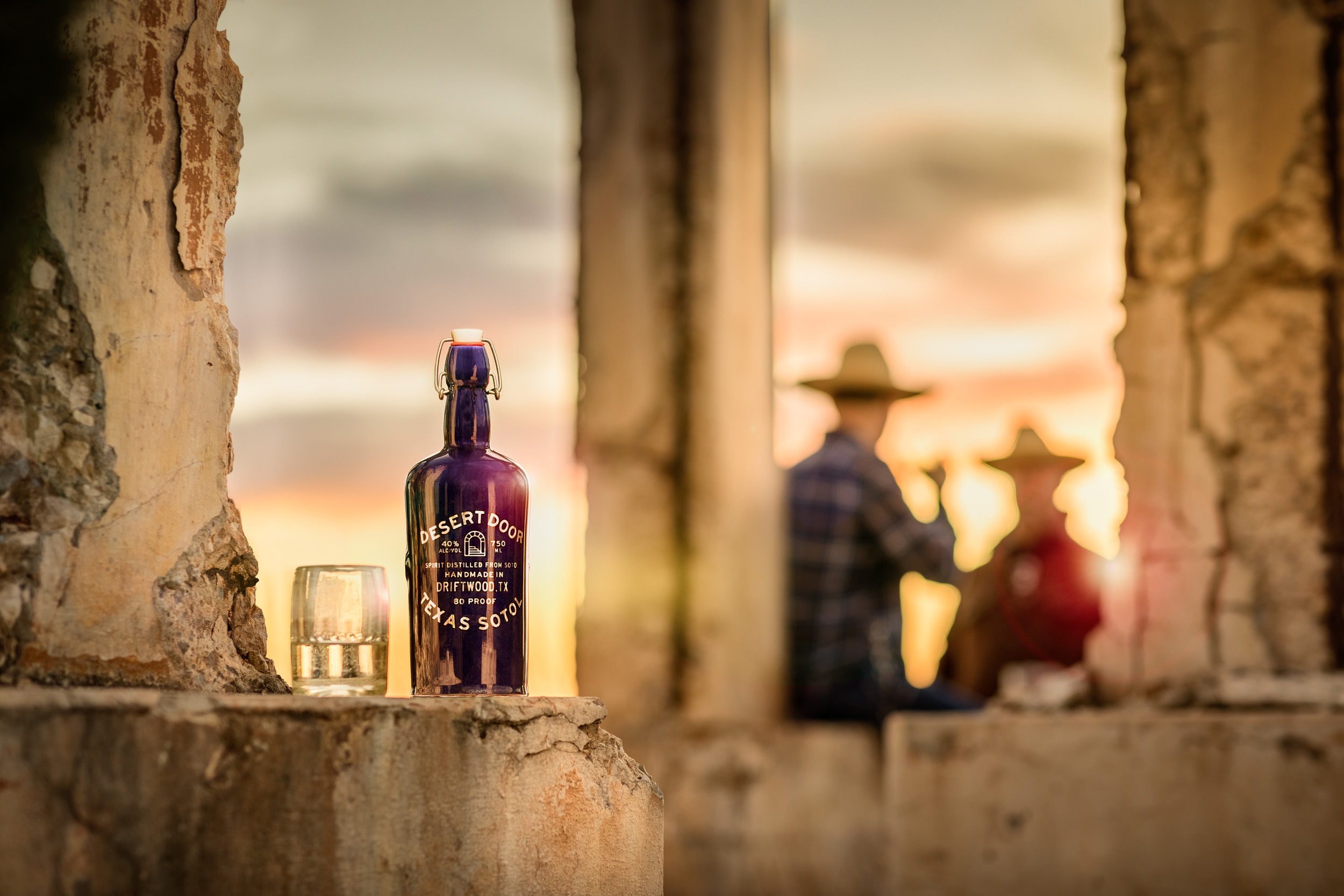 bottle of desert door sotol on ledge with two men in background drinking