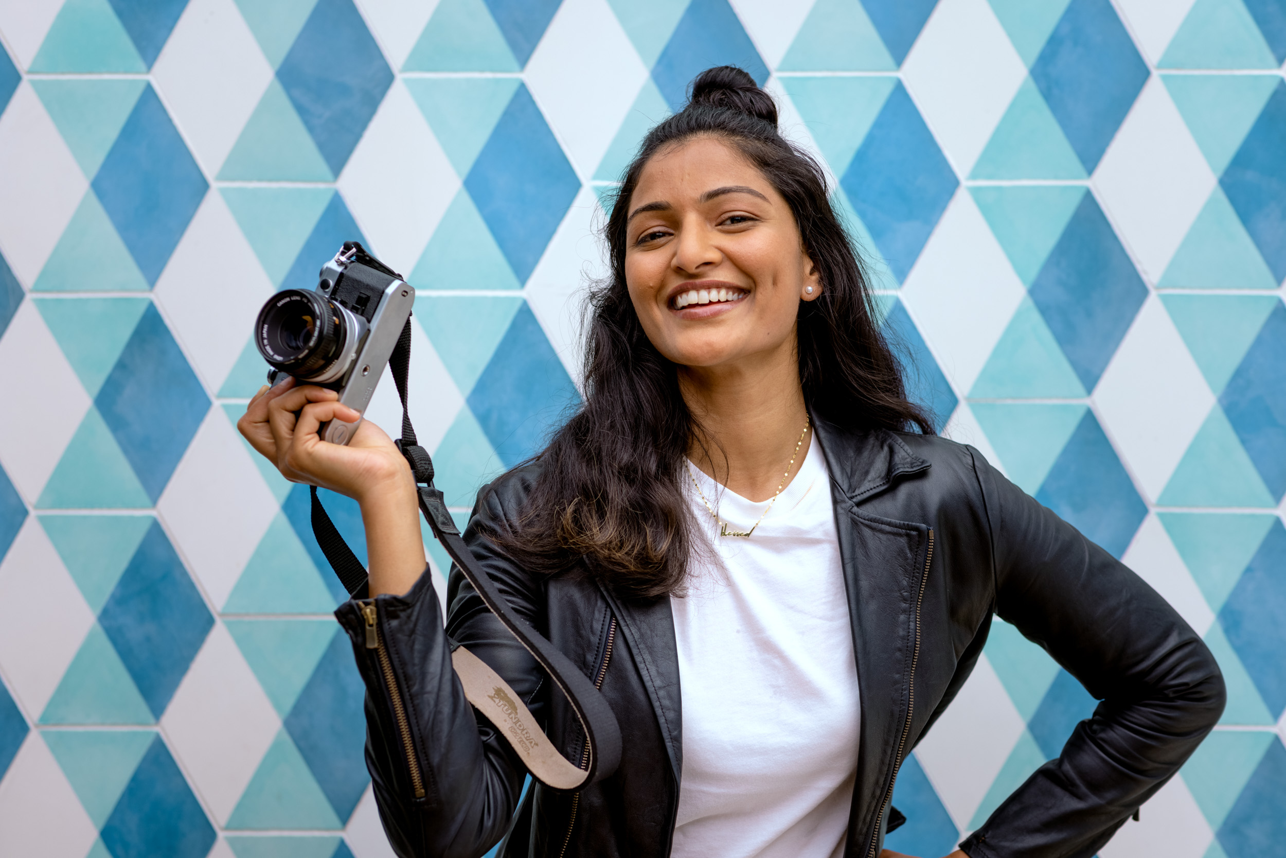 woman smiling and holding film camera in front of checkered pattern wall