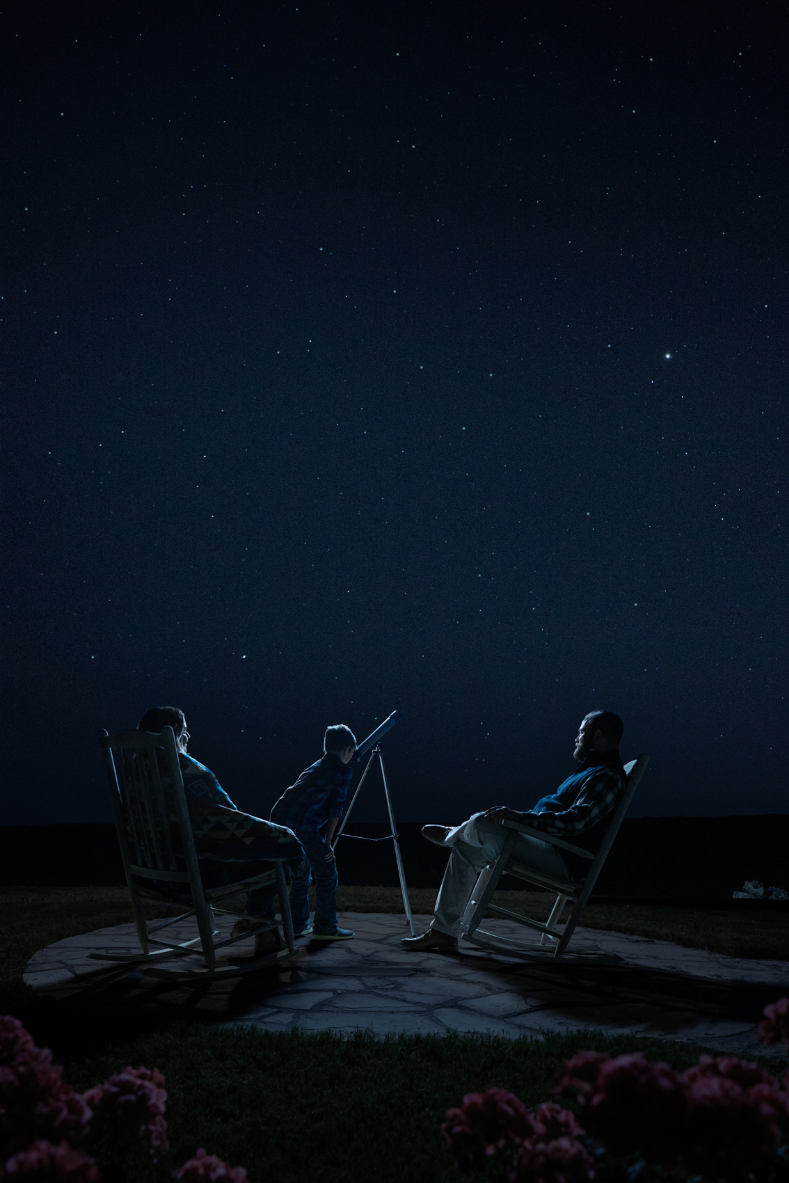 parents and young boy stargazing outside at night with telescope