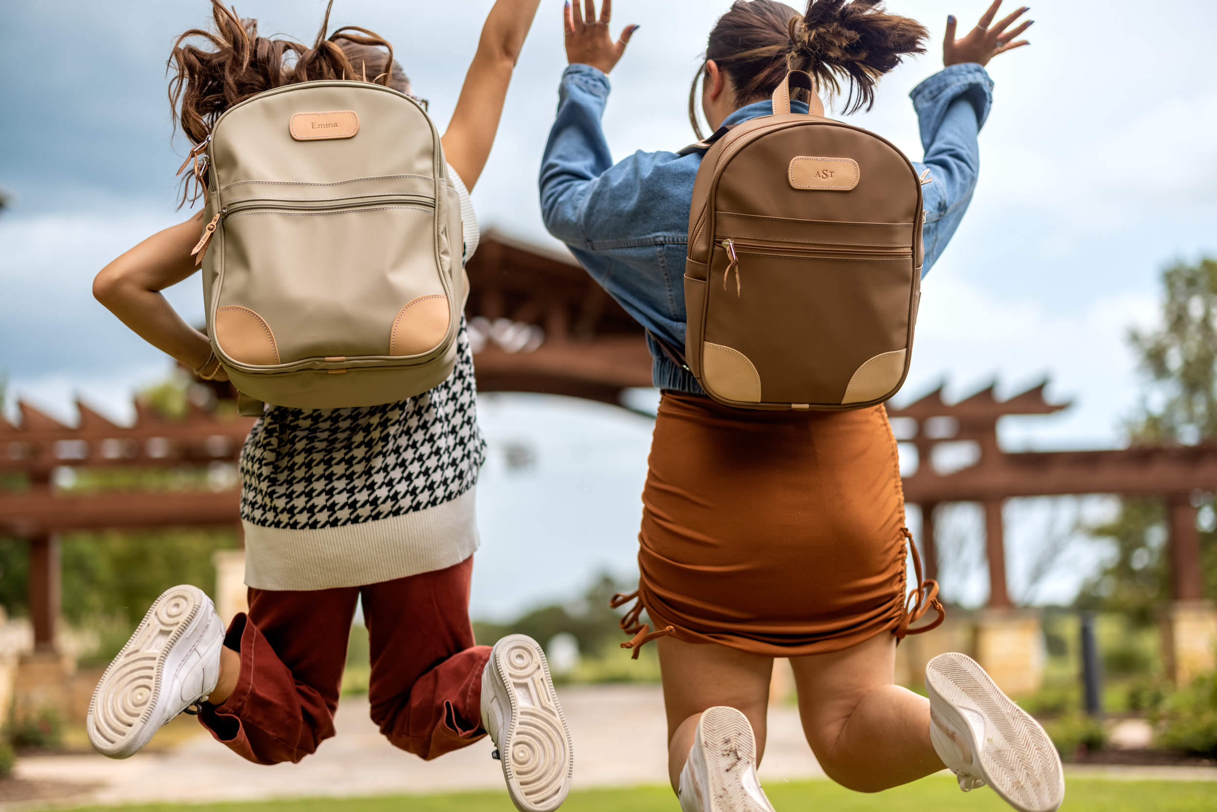 two girls jump in air wearing jon hart backpacks