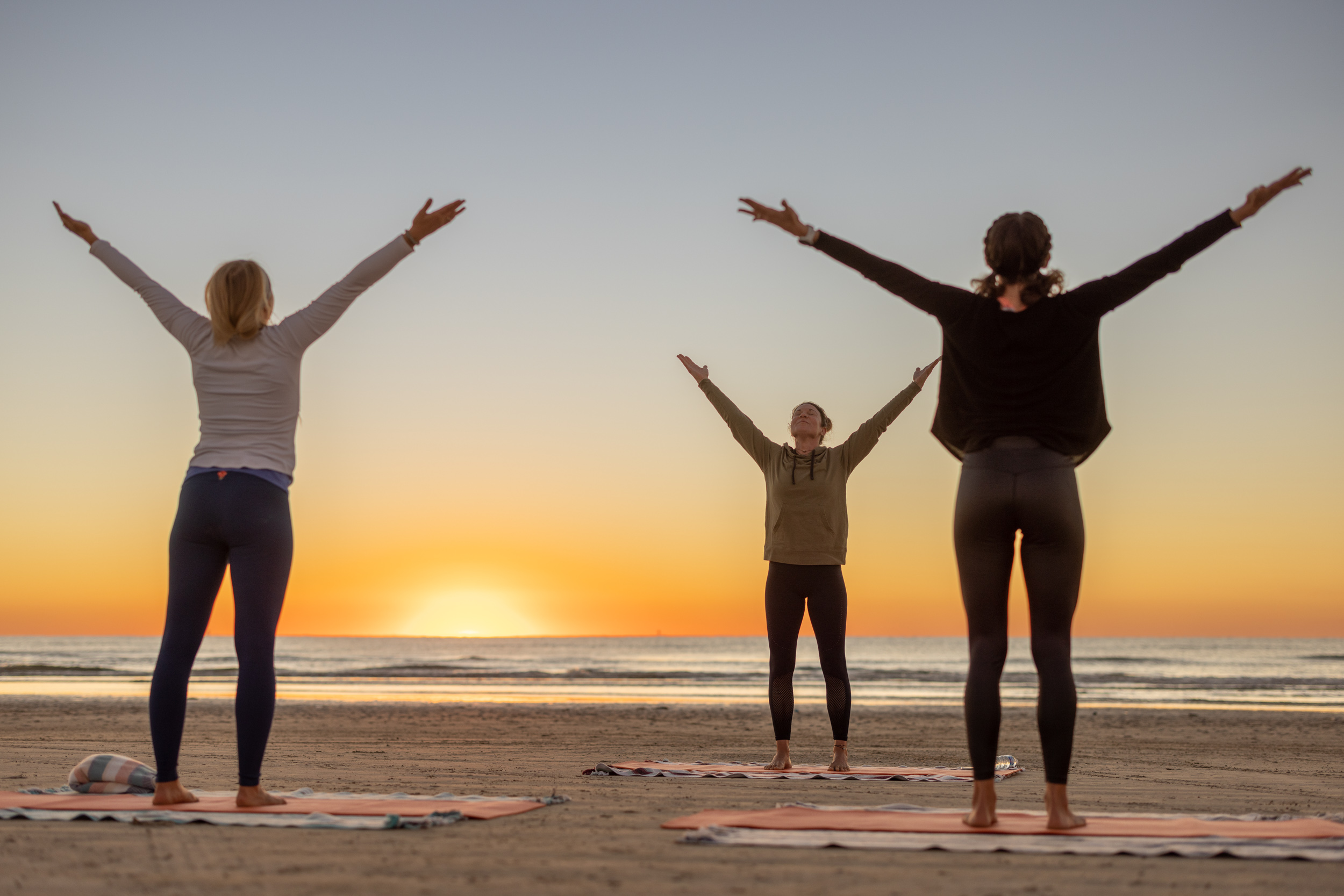 three women yoga posing at sunrise on texas gulf beach