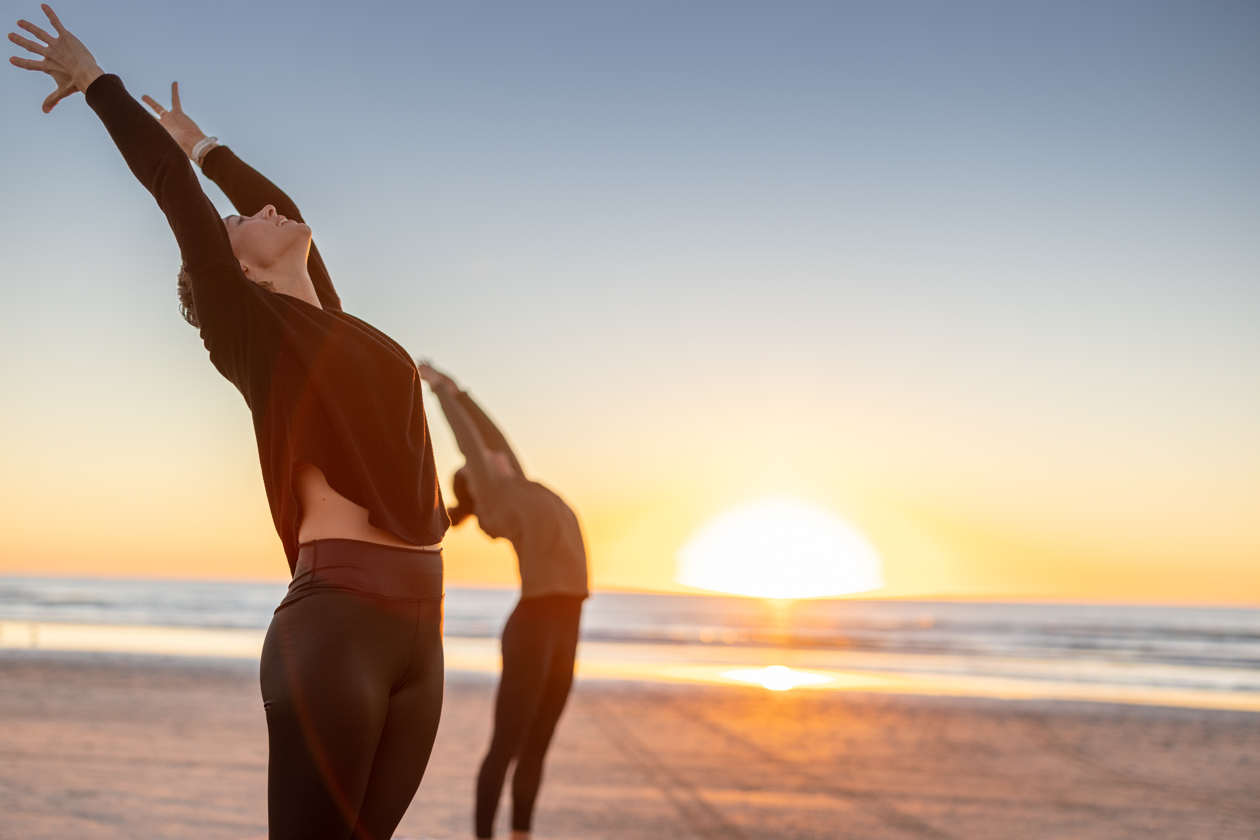 two women yoga posing at sunrise on beach