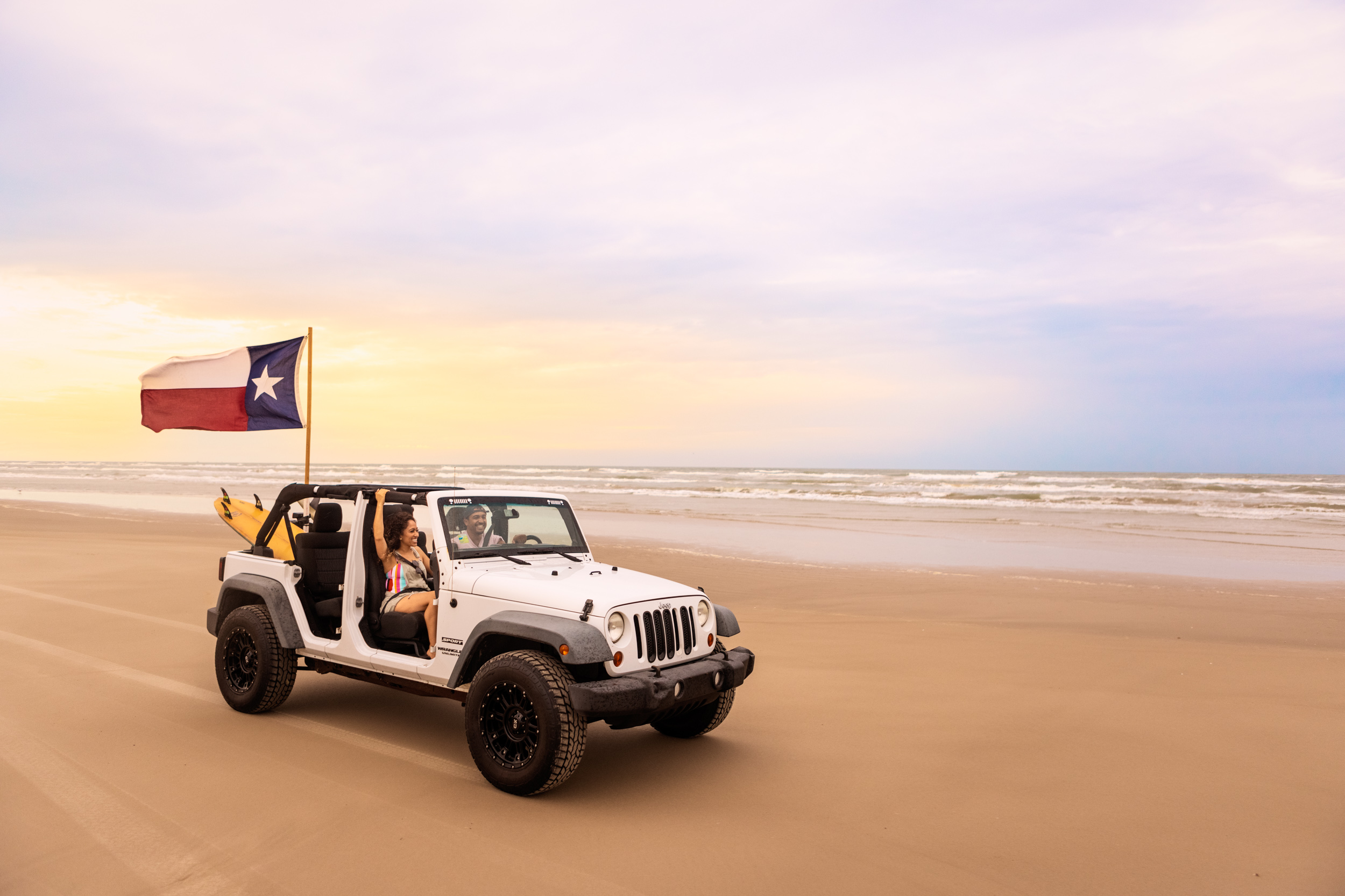 couple riding in jeep with texas flag on gulf coast beach