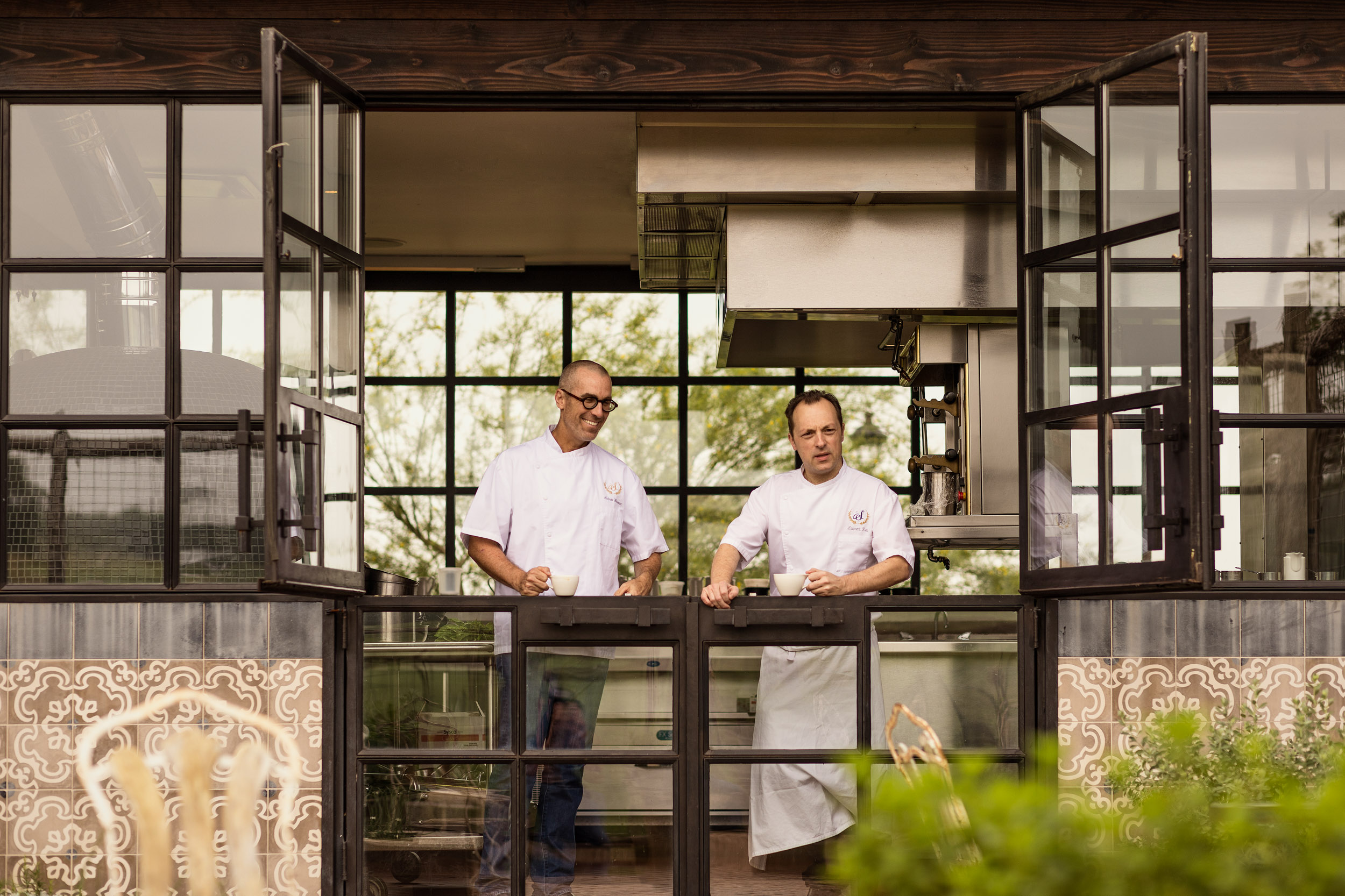two chefs look out window of restaurant kitchen