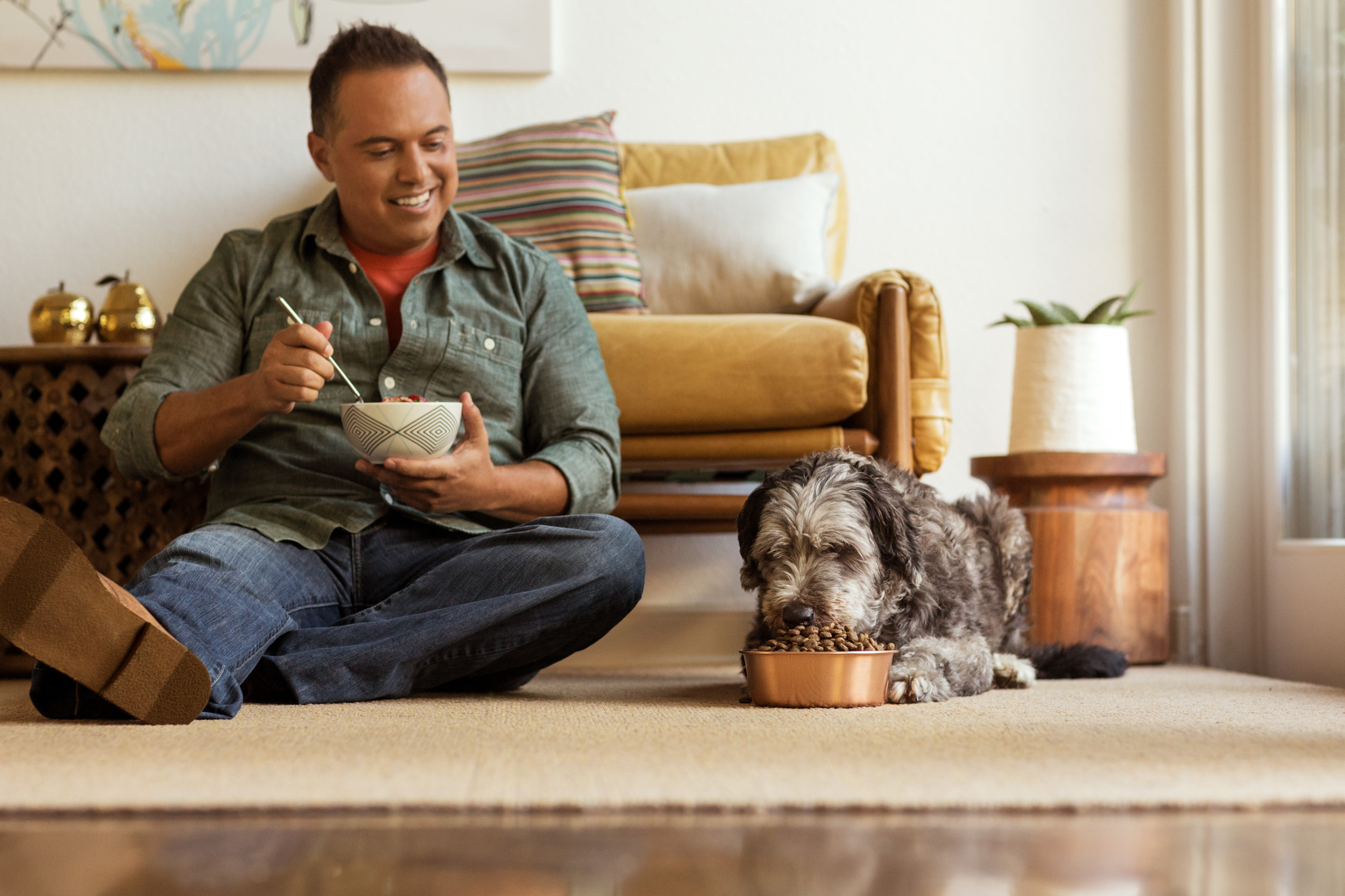 man and pet dog on floor eating together