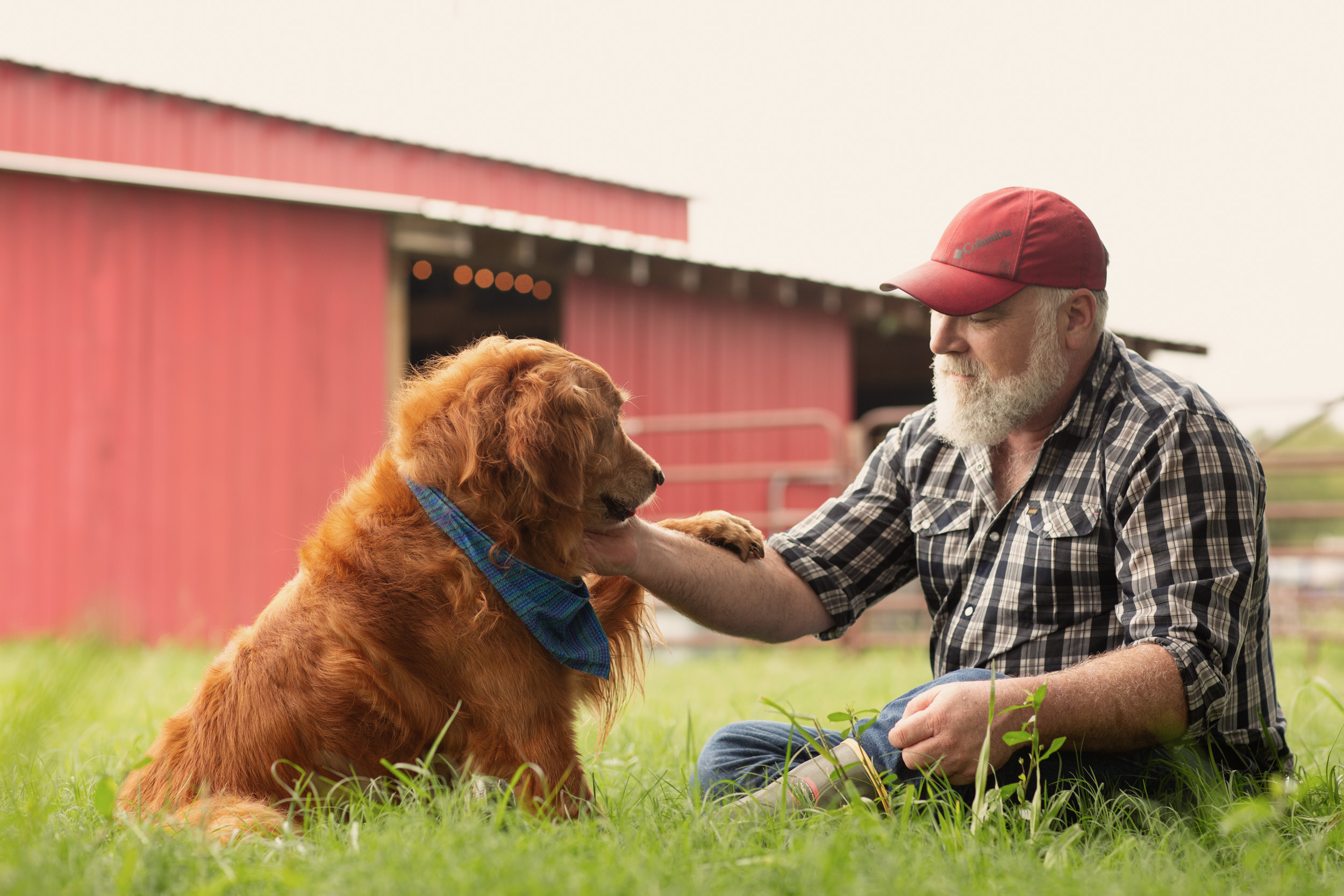 farmer sitting with dog with red barn in background
