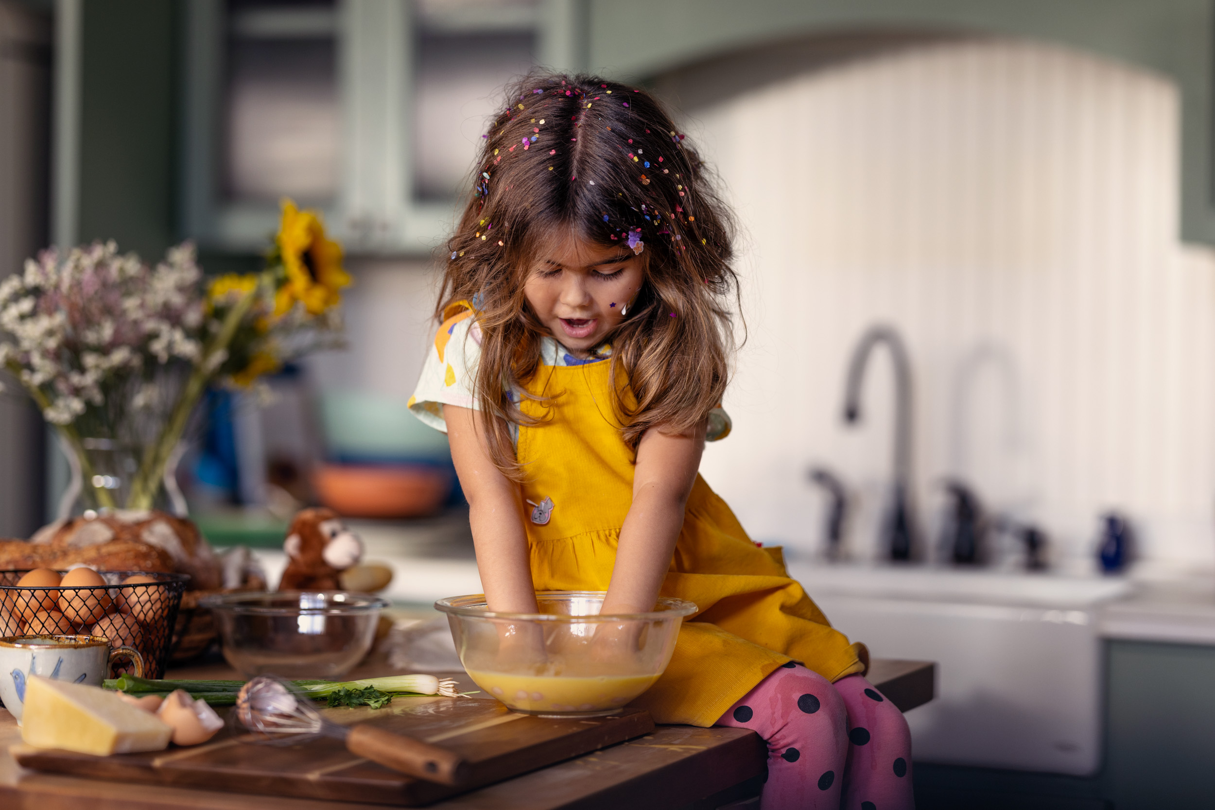 young girl with confetti in hair mixing food in bowl in kitchen