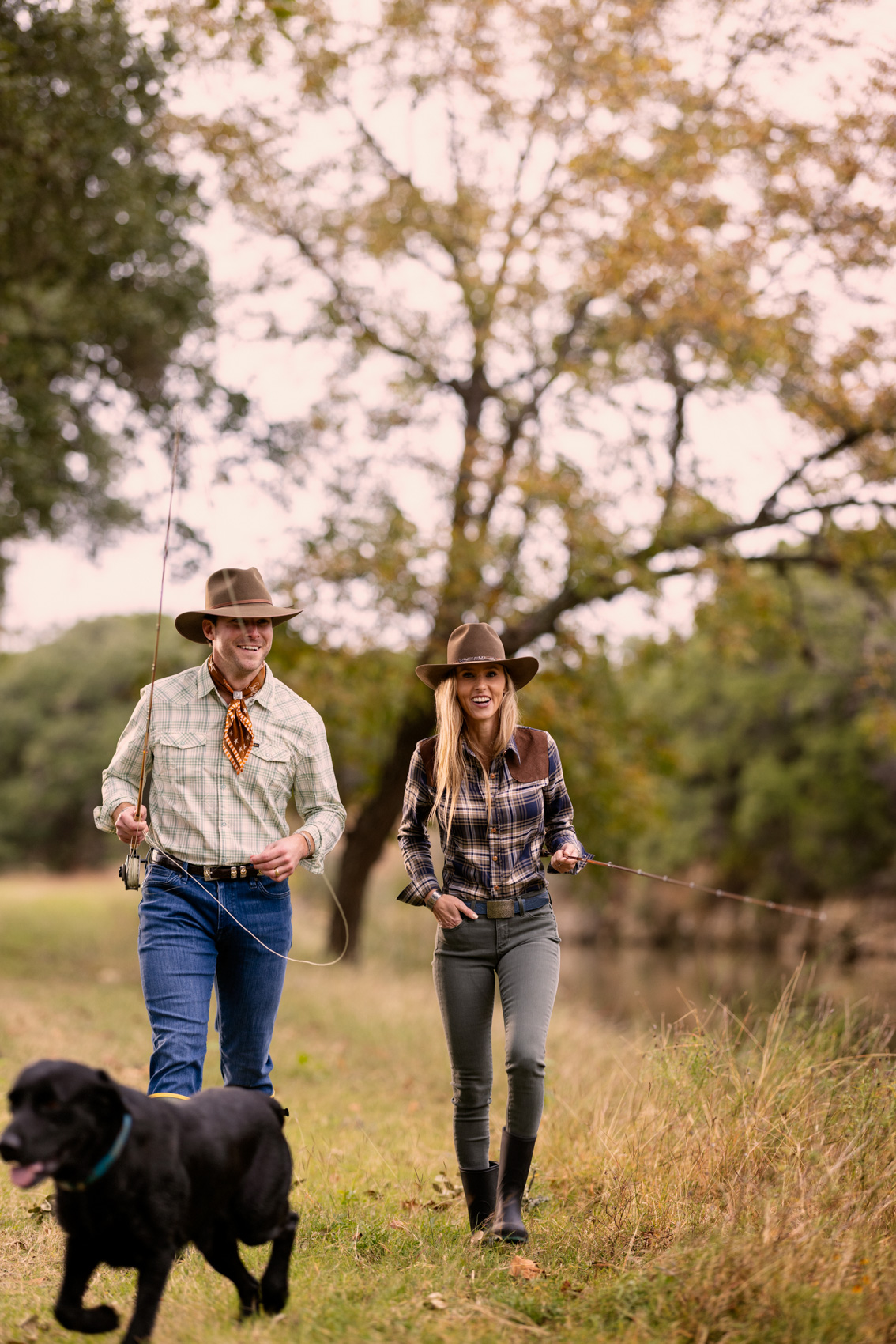 man and woman walking with fly fishing rods and black dog