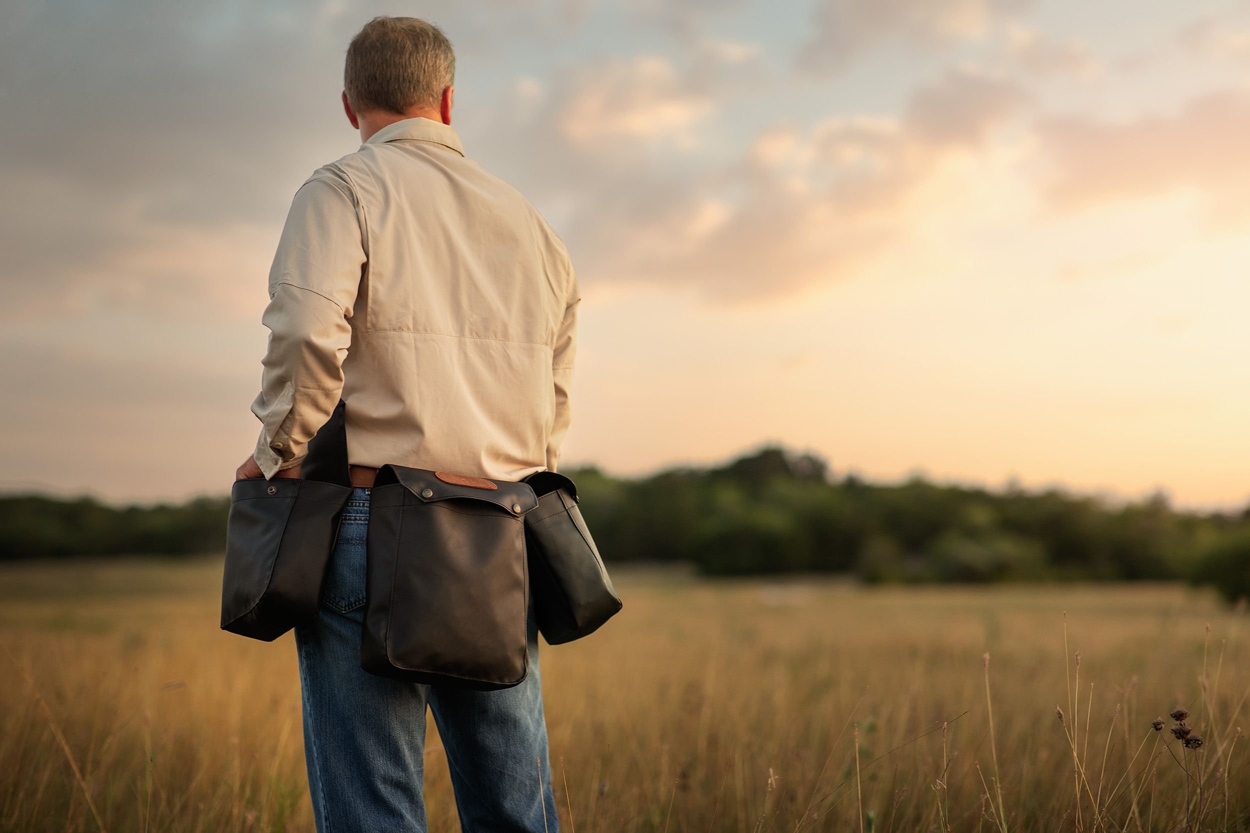 man standing in open field at sunset wearing jon hart shot gun shell bags