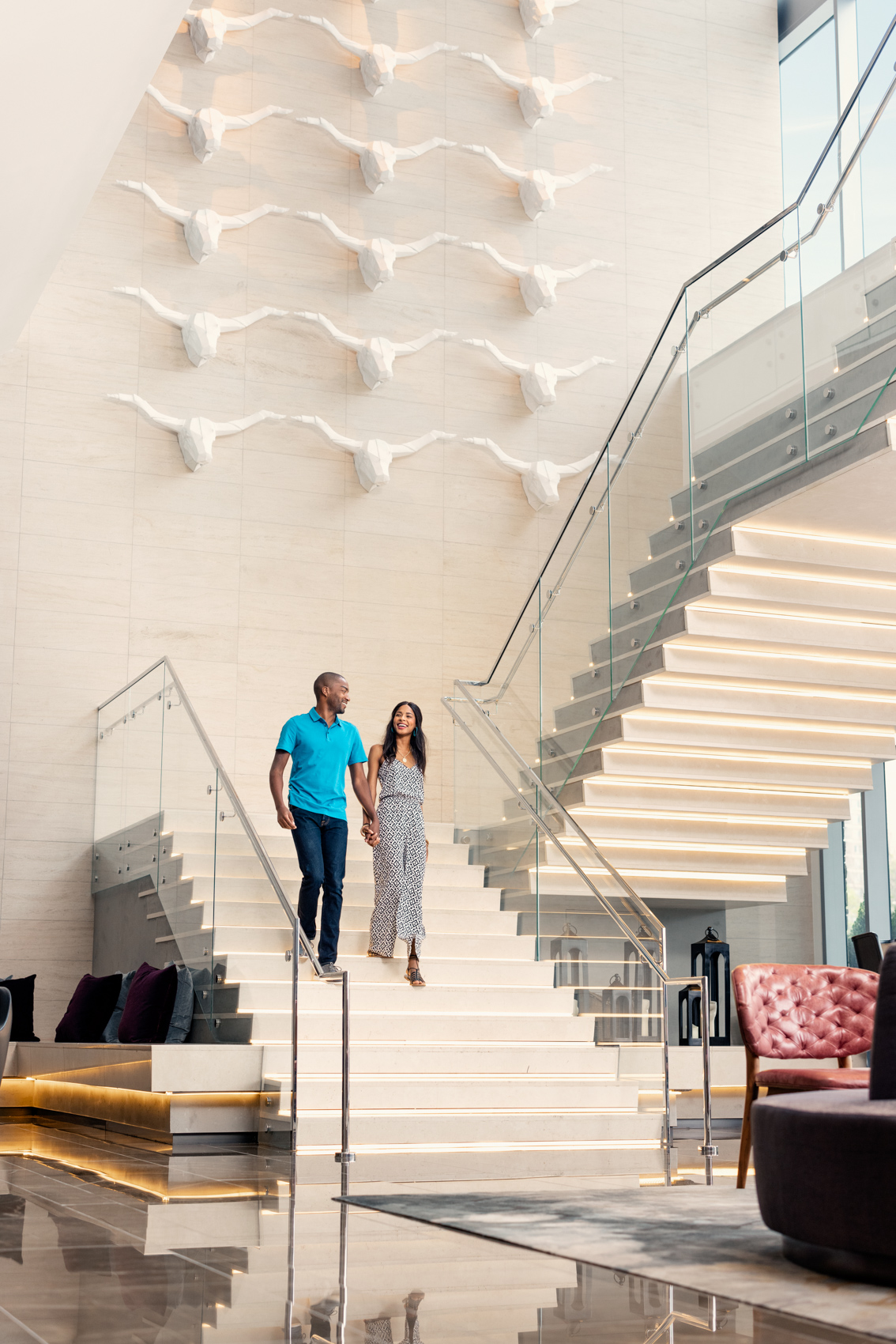 couple holding hands walking down large white staircase in hotel lobby