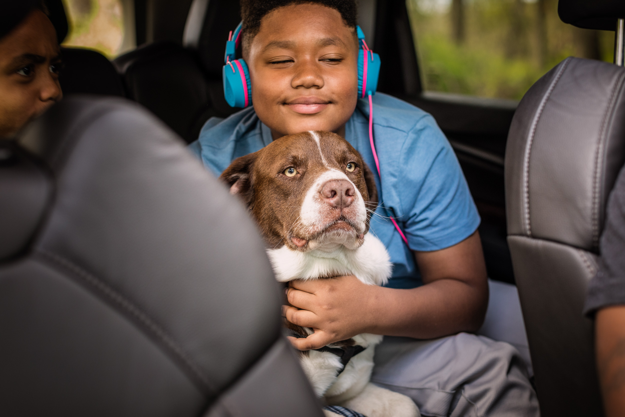 young boy wearing headphones hugging dog in car